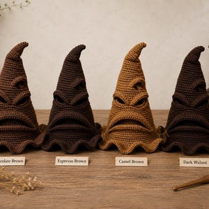 May include: Four crocheted pointed hats with expressive facial features including eyes and a mouth. The hats are labeled Chocolate Brown, Espresso Brown, Camel Brown, and Dark Walnut, showcasing different shades of brown yarn in a textured stitch.