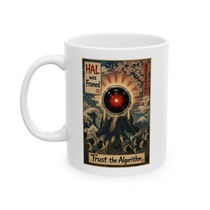 May include: White ceramic mug featuring a retro-style graphic with the text "HAL was Framed" and "Trust the Algorithm." The design includes a red eye, Japanese art elements, and a mountain scene. The mug has a curved handle.