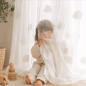 May include: A sheer white curtain panel featuring a repeating pattern of soft, rounded cloud shapes. The fabric is lightweight and translucent, allowing light to filter through while displaying the cloud motifs across the surface of the material.