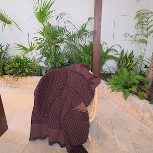May include: A dark maroon knit sweater with a textured waffle pattern and a solid-colored collar. The garment features a distinct triangular patch detail on the chest area and a ribbed hemline, showcasing a structured design and long sleeves.