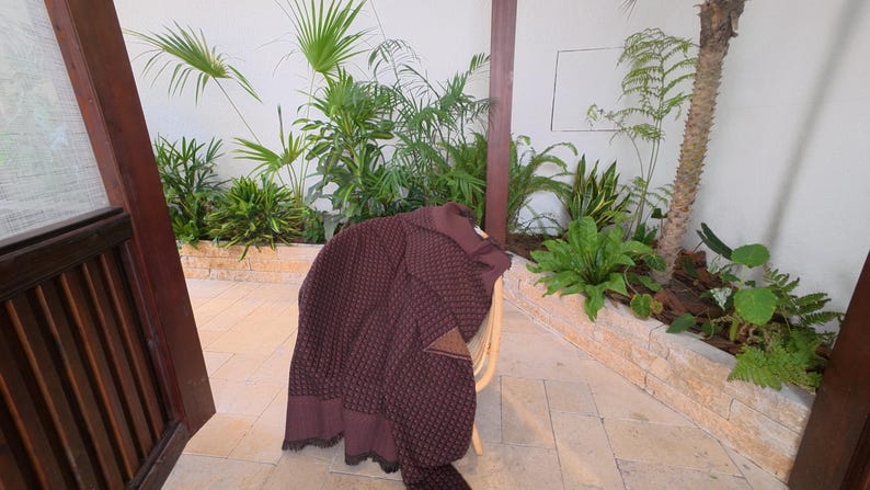 May include: A dark maroon knit sweater with a textured waffle pattern and a solid-colored collar. The garment features a distinct triangular patch detail on the chest area and a ribbed hemline, showcasing a structured design and long sleeves.