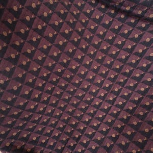 May include: A fabric cushion featuring a repeating geometric pattern of dark brown and black triangles arranged in a grid. Each triangle contains a small, centered tan dot, creating a textured appearance across the surface of the textile material.