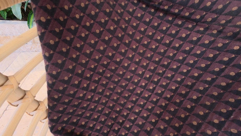 May include: A fabric cushion featuring a repeating geometric pattern of dark brown and black triangles arranged in a grid. Each triangle contains a small, centered tan dot, creating a textured appearance across the surface of the textile material.