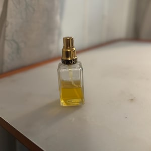 May include: A small, rectangular perfume bottle with a gold-coloured cap and the brand name "CHANEL" printed on it. The bottle contains a yellow liquid. The bottle is on a white surface.