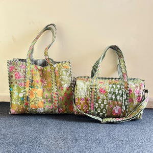 以下が含まれることがあります： 緑、ピンク、白の花柄パッチワークが施されたキルティング生地の長方形トートバッグと円筒形ダッフルバッグ。どちらのバッグにも、緑と白のストライプ柄の生地で作られた持ち手と縁取りが付いています。