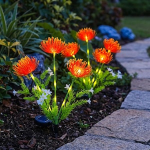 Pode incluir: Um conjunto de luzes solares de jardim em forma de lírios-aranha cor de laranja com caules verdes e pequenas flores brancas. Cada flor emite uma luz quente, suportada por caules verdes finos e uma base com painel solar preto.