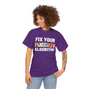 May include: A purple short-sleeve t-shirt featuring the white text FIX YOUR ALGORITHM printed on the front. The word FUCKING is displayed in the center using a variety of colorful, patterned letters in a collage style against the purple fabric.