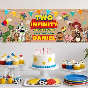 May include: A rectangular birthday banner featuring Toy Story characters, colorful bunting, and the text TWO INFINITY AND BEYOND HAPPY BIRTHDAY DANIEL. The banner is displayed above a table with a white cake, cupcakes, and cookies.