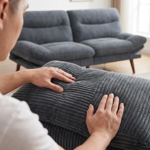 May include: A grey corduroy sofa and matching ottoman. The sofa has a two-cushion design with a curved back and wooden legs. The ottoman is rectangular and has a tufted design. The furniture is in a living room setting.