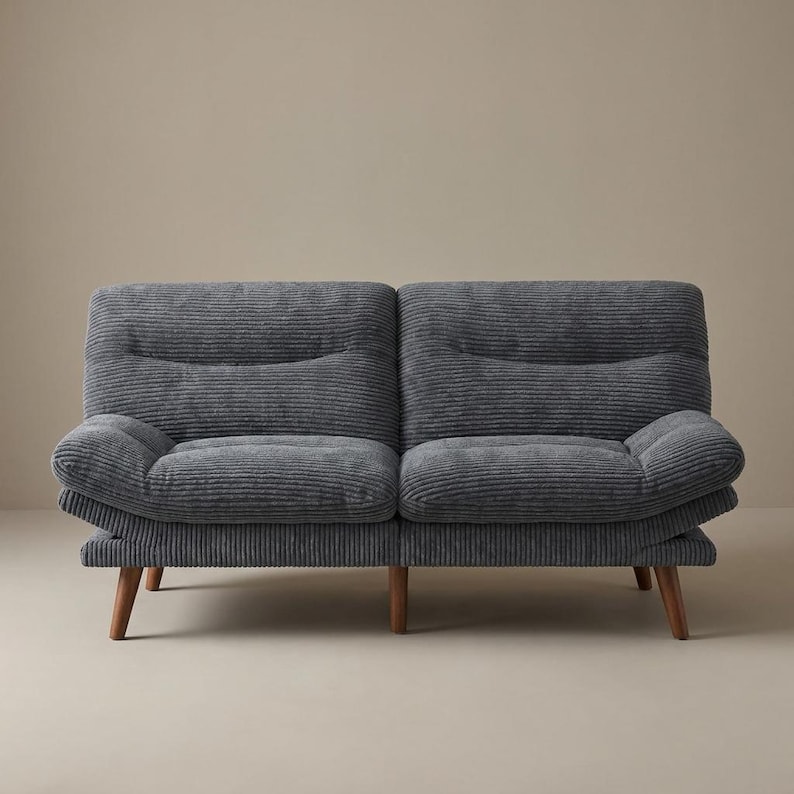 May include: A grey corduroy two-seater sofa with wooden legs. The sofa has a ribbed texture and a rounded arm design. The neutral colour and simple design make it suitable for various interior styles.