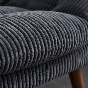 May include: Close-up of a section of a grey corduroy chair. The fabric has a ribbed texture, with the ridges running vertically. The colour is a muted grey, and the fabric appears soft and plush. The chair's wooden legs are visible.