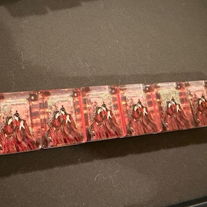 May include: A horizontal row of eight rectangular clear acrylic blocks, each featuring an identical printed illustration of two figures in traditional red robes standing together against a background of golden lanterns and architectural structures.