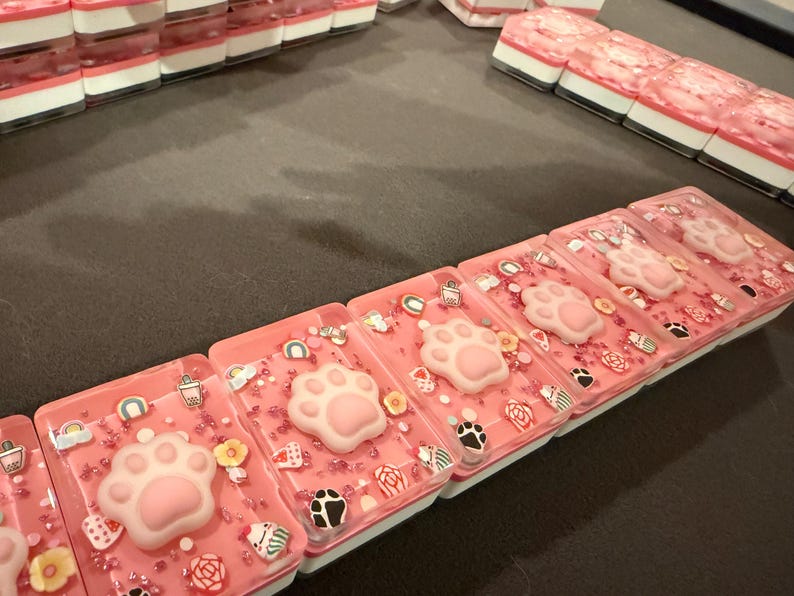 May include: Rectangular pink wax melts featuring a raised light pink cat paw print in the center. The surface is decorated with small colorful sprinkles, including tiny rainbows, flowers, and animal-themed shapes embedded in the wax.