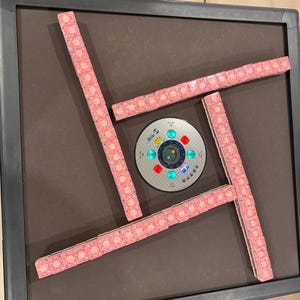 May include: A square automatic mahjong table with a dark brown felt surface and a black frame. Four rows of pink patterned mahjong tiles are arranged in a square formation around a central circular control panel with glowing green and red lights.