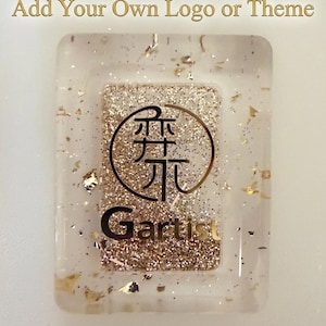May include: A rectangular clear resin piece with gold glitter and metallic flakes embedded inside. The center features a circular logo with Asian characters and the text "Gartist" in black. Above the piece, the text reads "100% Customizable: Add Your Own Logo or Theme."