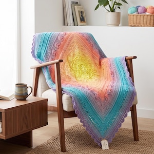 May include: A colorful, crocheted blanket draped over a wooden chair. The blanket features a gradient of colors, including yellow, orange, blue, and purple. The chair is made of wood and has a light-colored cushion. The blanket has a scalloped edge.