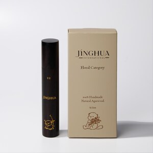 Peut inclure: Un étui cylindrique en bois brun foncé marqué 02 et JINGHUA avec un petit motif de loutre dorée, à côté d'une boîte rectangulaire beige marquée JINGHUA INTERNATIONAL, Floral Category, 100% Handmade Natural Agarwood, 10,5cm, et un motif de loutre.