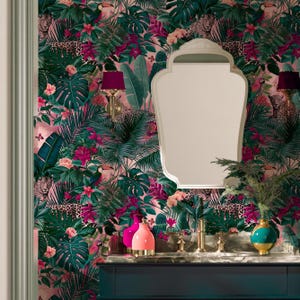 Peut inclure: Un mur recouvert de papier peint tropical avec un fond rose, des feuilles de palmier vertes, des fleurs d'hibiscus roses, des toucans et des léopards. Un miroir à cadre blanc est suspendu au-dessus d'un meuble sombre avec un robinet doré.