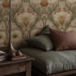 May include: A low-profile floor bed with olive green linen bedding and a dark terracotta pillow. Beside it, a rustic wooden side table holds two small ceramic vases on a book, next to a tall metal floor lamp against floral wallpaper.