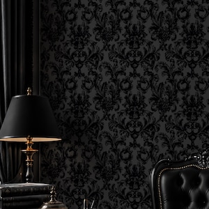 May include: A dark, elegant office setting featuring a black desk, a leather chair, and a lamp with a gold base. The wall is covered in a black damask wallpaper. Decorative items include books and a small container.