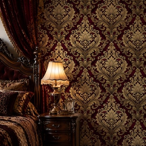 May include: A bedroom scene featuring a burgundy and gold damask wallpaper. A dark wood nightstand with a lamp and framed photo sits beside a bed with a patterned comforter and burgundy curtains.