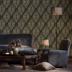 Puede incluir: Un interior de habitación con papel tapiz verde oscuro con un patrón de damasco dorado repetitivo. El espacio incluye un sofá de terciopelo gris oscuro, un sillón a juego, una mesa de centro de madera con un jarrón, una lámpara de pie y una alfombra marrón.