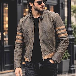 May include: A distressed brown leather jacket featuring a stand-up collar, a front zip fastening, and three horizontal tan stripes on each sleeve. The jacket includes two diagonal zipped pockets on the chest and a tan leather panel at the hem.