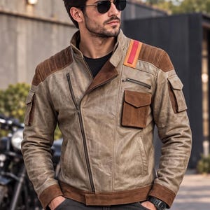 May include: A tan leather jacket featuring dark brown suede shoulder panels, cuffs, and pocket flaps. The jacket includes an asymmetrical zip closure, a stand-up collar, and a prominent red and orange vertical stripe detail on the left shoulder.