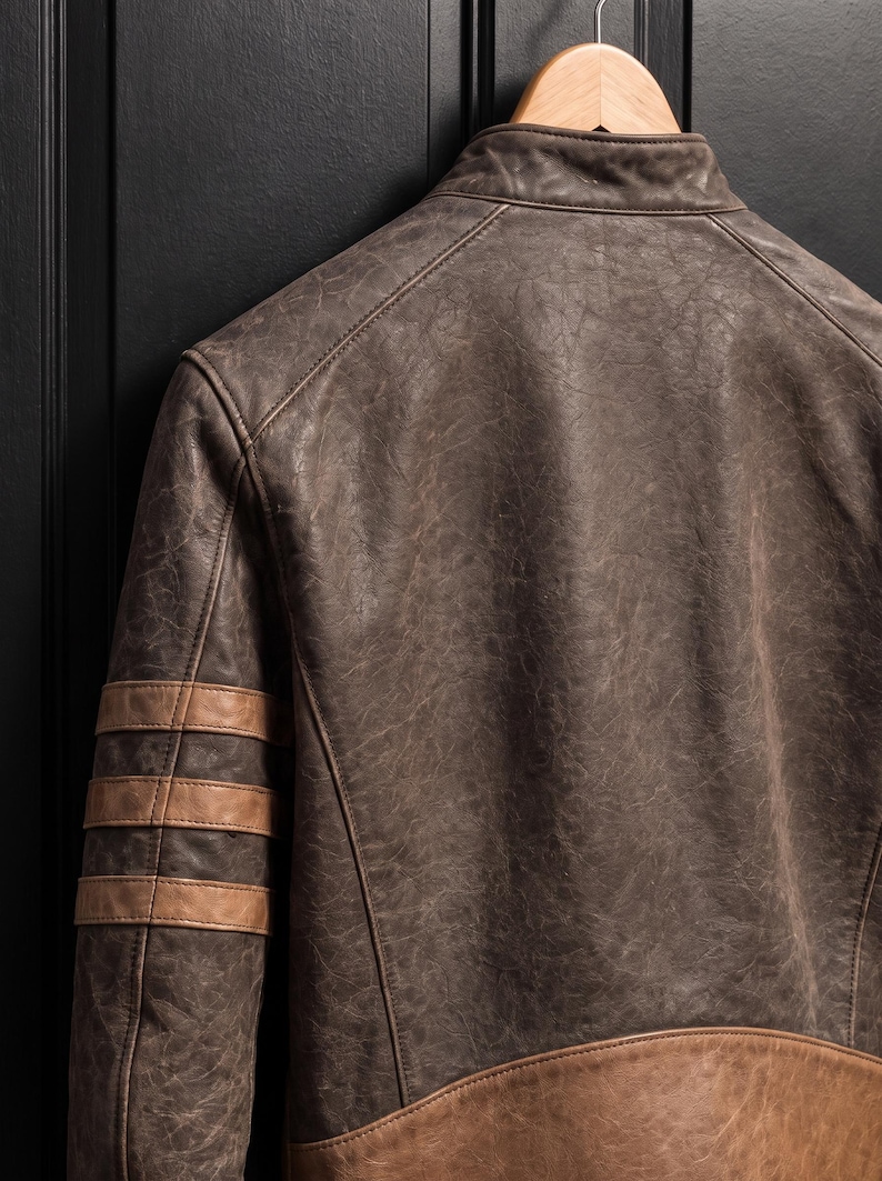 May include: A distressed dark brown leather jacket featuring a stand-up collar, three horizontal tan leather stripes on the upper sleeve, and a wide tan leather panel along the lower back hem, all constructed with visible reinforced stitching.