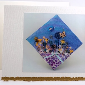 May include: A handmade greeting card with a blue and purple watercolor background. The card features a diamond-shaped design with a purple and white lace border. The center of the design features a cluster of yellow, orange, and white flowers with a blue butterfly.