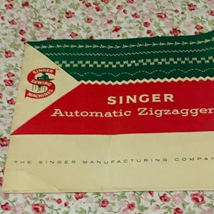 May include: A square instruction manual for a Singer Automatic Zigzagger. The cover features a green top section with white stitch patterns, a red middle section with white text, and a cream bottom section with the text The Singer Manufacturing Company.