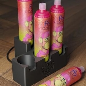 Könnte beinhalten: Vier glitzernde, rosa-gelbe zylindrische Flaschen mit rosa Kappen, die ein Cartoon-Affen-Design zeigen. Die Flaschen befinden sich in einem dunkelgrauen Halter mit dem Text "O.B.R. A-TEN". Eine Flasche liegt auf der Oberfläche.