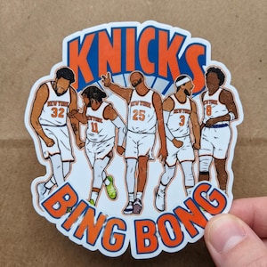 May include: A sticker featuring a cartoon illustration of five basketball players in white and orange uniforms. The word "Knicks" is arched across the top in blue and orange, with "Bing Bong" below. The players are in various poses.