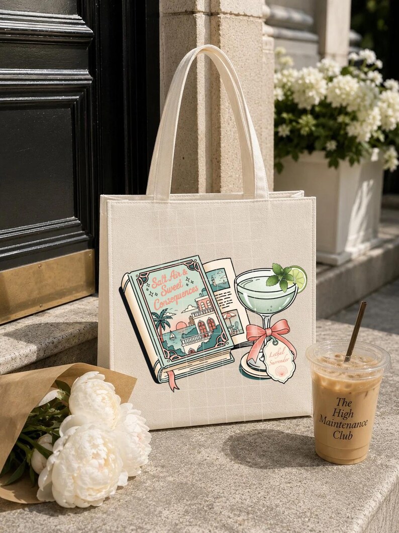 May include: A cream-colored canvas tote bag featuring a graphic print of an open book titled Salt Air & Sweet Consequences, a cocktail glass with a lime slice and a pink bow, and a small tag labeled Lathel Serenade with a seashell icon.