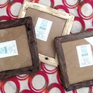 May include: Three square wooden picture frames with a rustic finish. Two frames are dark brown, and one is light natural wood. Each frame features a white label with the text DW Frames and More, indicating a size of 8 inches by 8 inches.