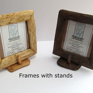 May include: Two square wooden picture frames with stands, one light-toned and one dark-toned. Each frame features a textured, rustic border and contains a white insert with the text DW FRAMES AND MORE, 4"x4", and 150mm x 150mm. The frames are supported by small, matching wooden bases.