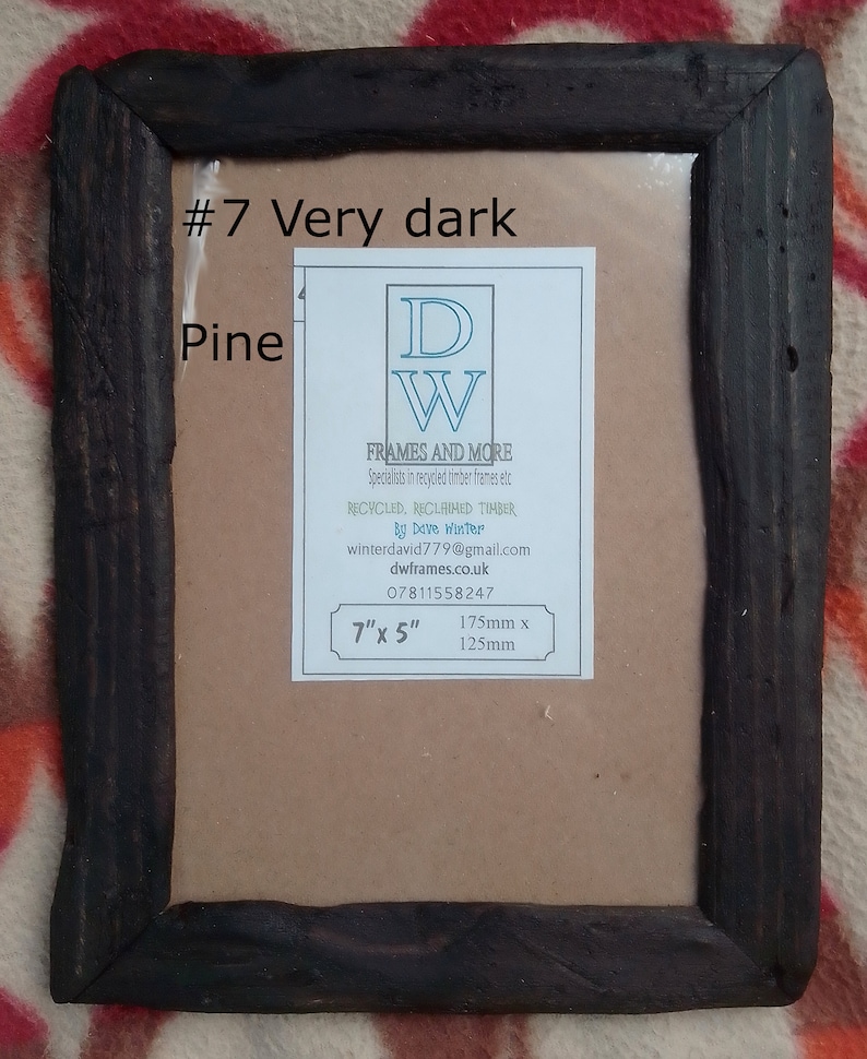 May include: A rectangular picture frame made of very dark pine wood with a rustic texture. A white label is centered inside, reading #7 Very dark Pine, DW FRAMES AND MORE, Recycled, Reclaimed Timber by Dave Winter, and 7" x 5" (175mm x 125mm).
