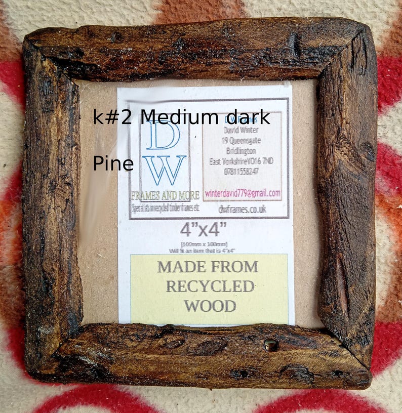 May include: A square picture frame crafted from dark, textured recycled pine wood. The frame features a label with the text k#2 Medium dark Pine, 4"x4", and MADE FROM RECYCLED WOOD, along with contact details for DW Frames and More in Bridlington.