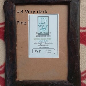 May include: A rectangular picture frame made of dark brown reclaimed pine wood with a rough, textured finish. A white label is centered on the backing, featuring the text #8 Very dark Pine, DW FRAMES AND MORE, and dimensions of 7 inches by 5 inches.