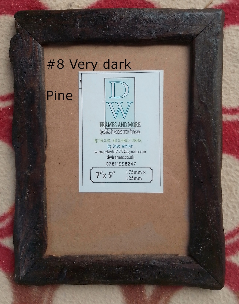 May include: A rectangular picture frame made of dark brown reclaimed pine wood with a rough, textured finish. A white label is centered on the backing, featuring the text #8 Very dark Pine, DW FRAMES AND MORE, and dimensions of 7 inches by 5 inches.
