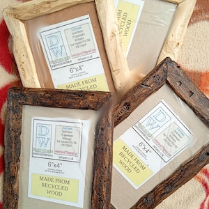 May include: Four rectangular picture frames made from recycled wood, featuring two light-colored frames and two dark-colored frames. Each frame contains a label stating 6"x4" and Made From Recycled Wood, along with contact details for D.W. Frames.