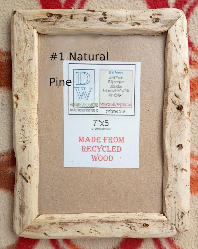 May include: A rectangular picture frame made from natural pine wood with a rough, textured finish. A label inside reads #1 Natural Pine, 7"x5", and MADE FROM RECYCLED WOOD, along with contact details for D.W. Frames and More in Bridlington.
