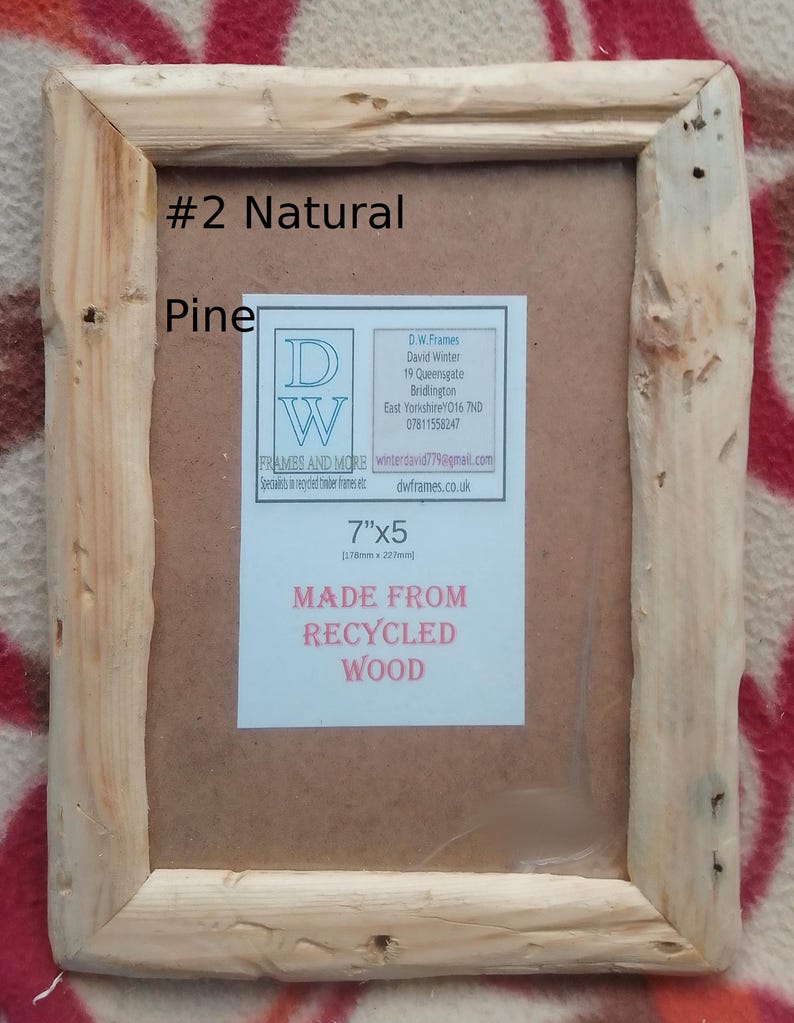 May include: A rectangular natural pine wood picture frame with a rough, unfinished texture. The frame contains a label with the text #2 Natural Pine, 7"x5", and MADE FROM RECYCLED WOOD, along with contact details for D.W. Frames and More.