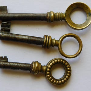 Peut inclure: Trois clés anciennes avec des poignées en laiton ornées et des tiges en métal sombre vieilli. Les clés varient en design, avec des anneaux circulaires et décoratifs. Les clés sont probablement des pièces vintage ou des reproductions.