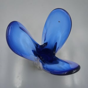 May include: A vibrant blue glass bowl featuring a unique three-lobed, petal-like design. The translucent material transitions from a deep, saturated cobalt blue at the center to a lighter, more transparent blue along the curved, rounded edges.