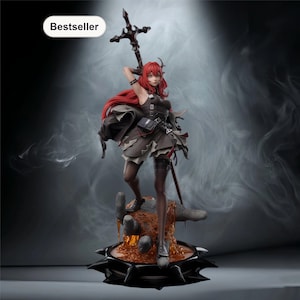 May include: A detailed figurine of a female character with long red hair, wearing a dark outfit and holding a cross-shaped weapon. The figure stands on a detailed base with a fiery, lava-like effect. The word "Bestseller" is in a white oval.