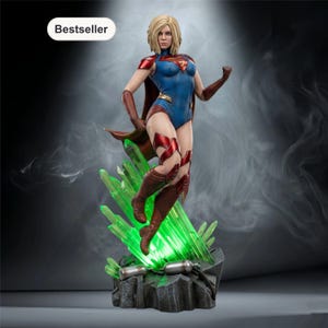 Puede incluir: Estatua de Supergirl en pose dinámica, con un traje azul y rojo con capa. La estatua está sobre una base con cristales verdes brillantes. La palabra "Bestseller" está en un óvalo blanco en la esquina superior izquierda.