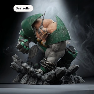 May include: A detailed statue of a muscular character in a crouching pose, featuring a green helmet and armor. The figure has a pale complexion, visible teeth, and is chained. The base is a rocky structure, and the word "Bestseller" is displayed.