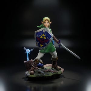 Può includere: Una statuetta dettagliata di un personaggio biondo con tunica verde, pantaloni bianchi e stivali marroni. Il personaggio impugna uno scudo blu con un emblema triforce giallo e una spada argentata. Una piccola fata blu luminosa e una bomba.