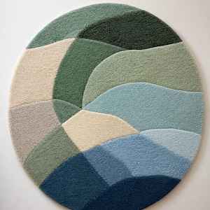 May include: A circular area rug featuring a tufted texture with an abstract pattern of curved, organic shapes in various shades of green, blue, beige, and grey. The design creates a layered, topographical effect across the entire round surface.